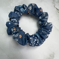 Nahaufnahme des Stoffes: jeansblaues Baumwoll-Scrunchie mit Blumen- und Schmetterlingsmuster – hochwertig verarbeitet